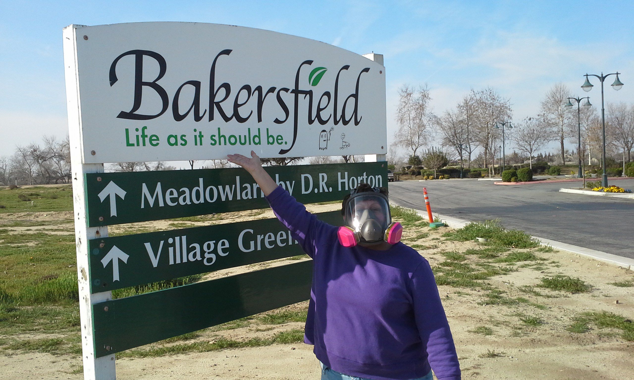 Person in filtering industrial face mask standing next to welcome sign for Bakersfield CA (Life as it should be)