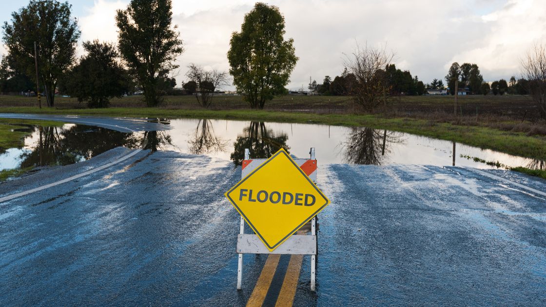 Image: A flooded road with a sign that says Flooded. Source: Canva