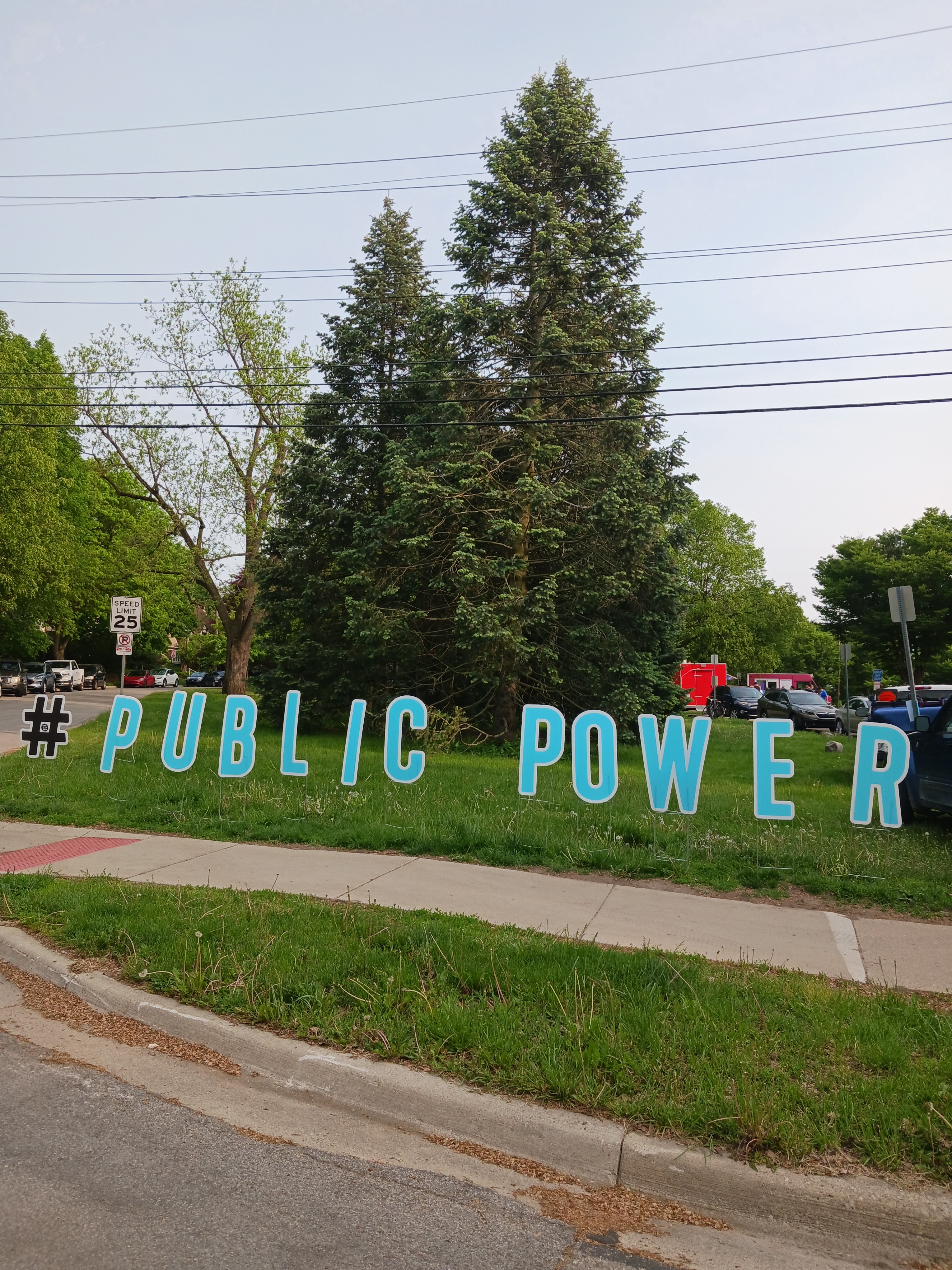 Large cut out letters spelling #PUBLICPOWER on grass outside Ann Arbor for Public Power rally, Burns Park 2023