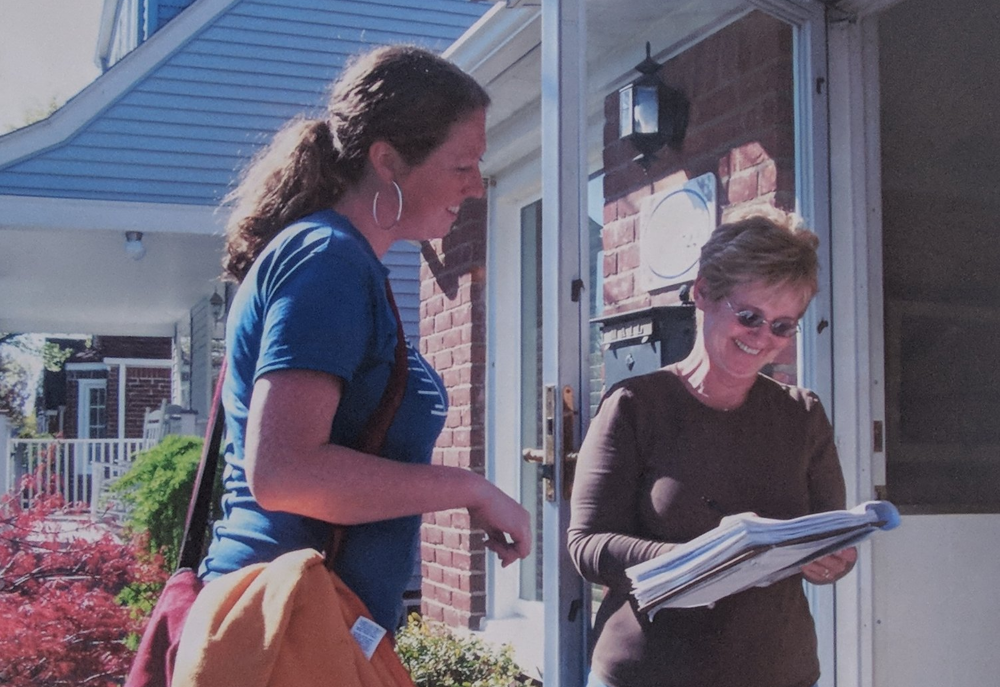 Two woman outside a home, one getting the other to sign a clipboard