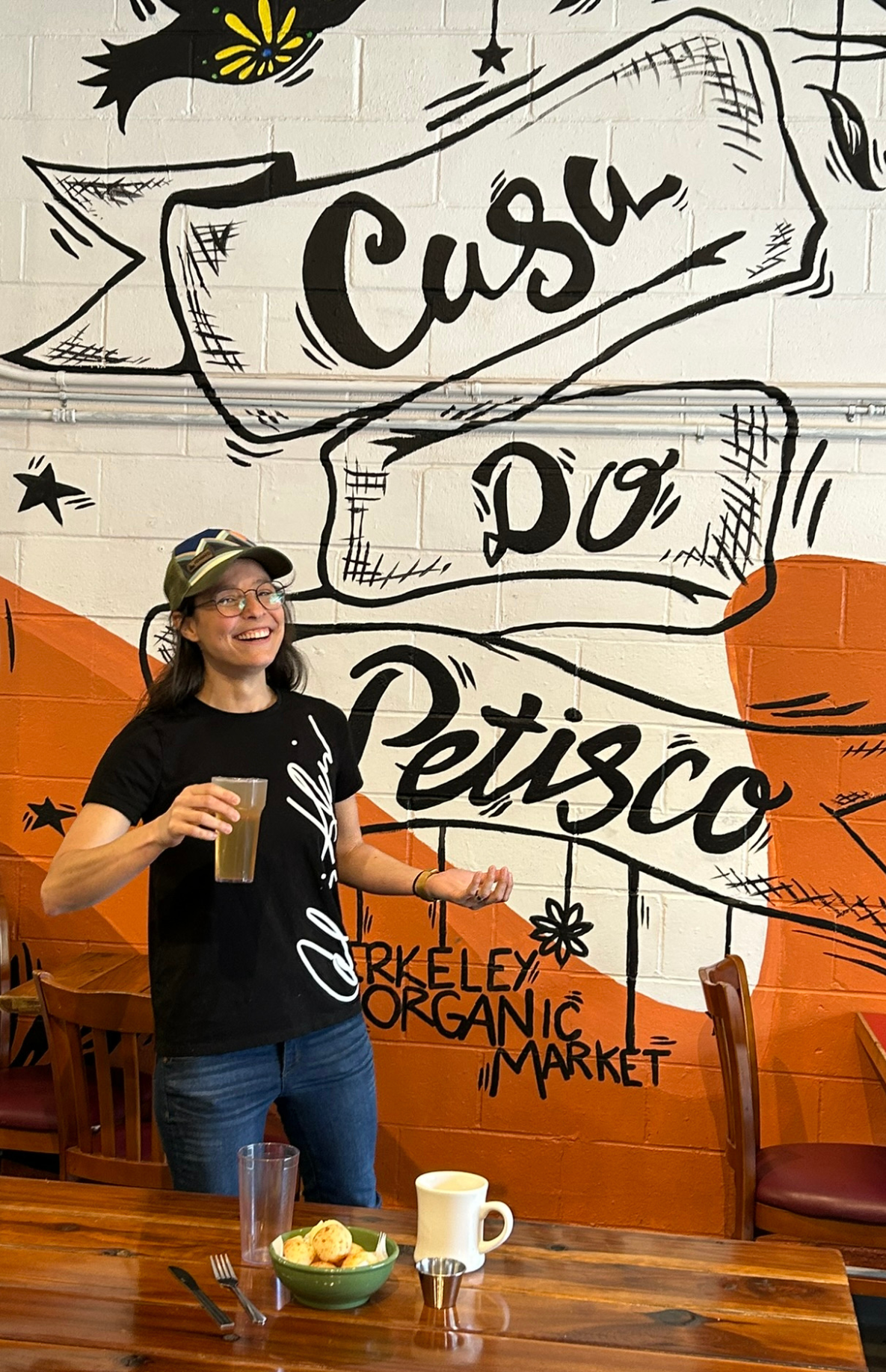 A staff person showing off reusable diningware before a wall mural that reads "Casa Do Pestisco"