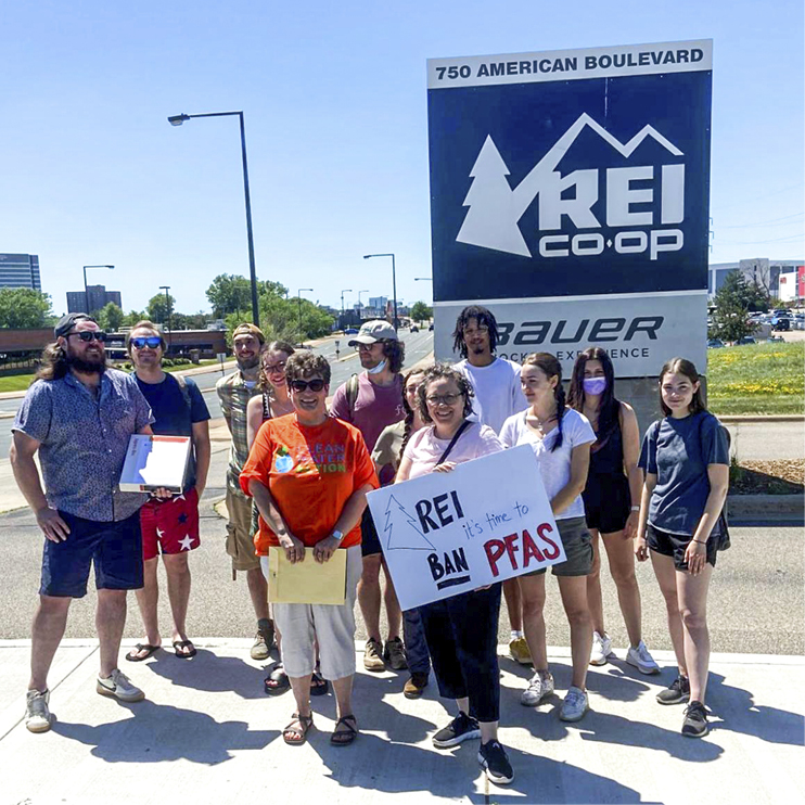 MN staff and members outside REI store sign with handmade "REI ban PFAS!" sign