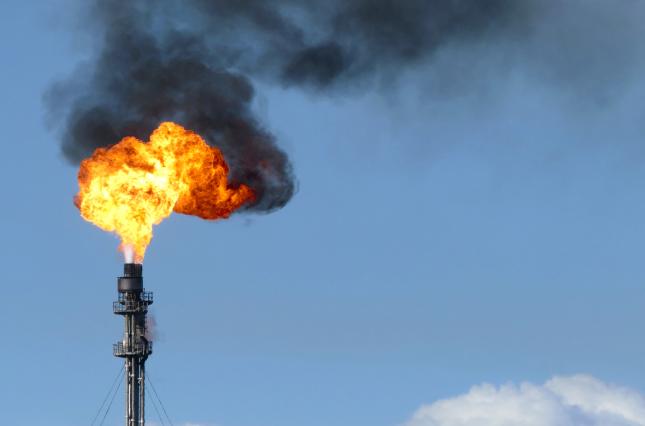 Gas flare fire and black smoke on blue sky day. 