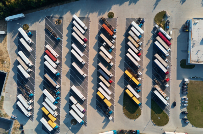Image of a bunch of trucks in a parking lot by a warehouse - Canva