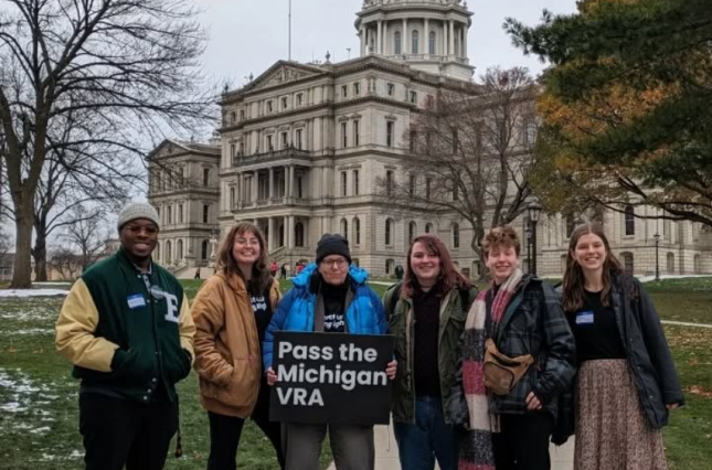 Group of people by Michigan Capitol holding sign "Pass the Michigan VRA"