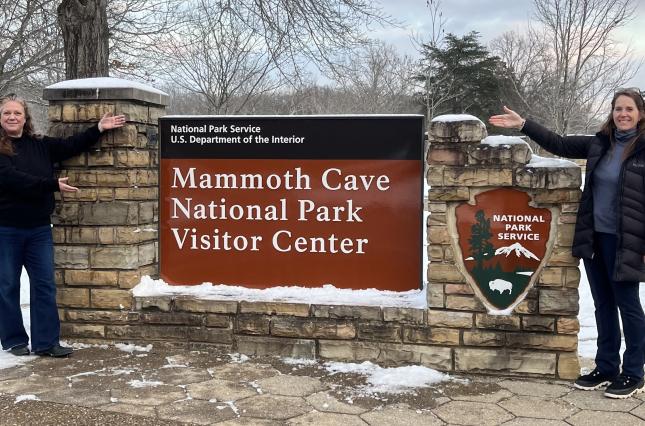 Two women next to the sign for the Mammoth Cave National Park Visitor Center