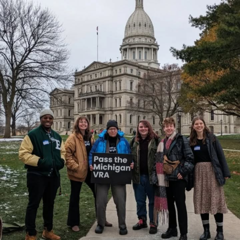 Group of people by Michigan Capitol holding sign "Pass the Michigan VRA"