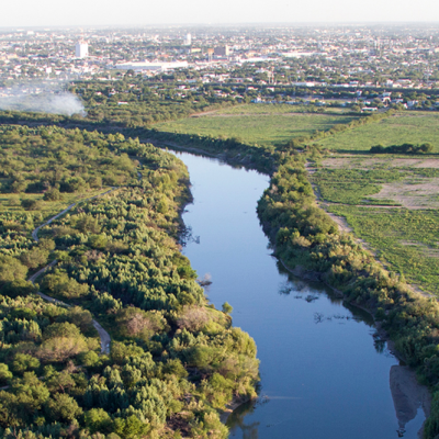 Rio Grande River cutting through forested land and farmland with city on the horizon