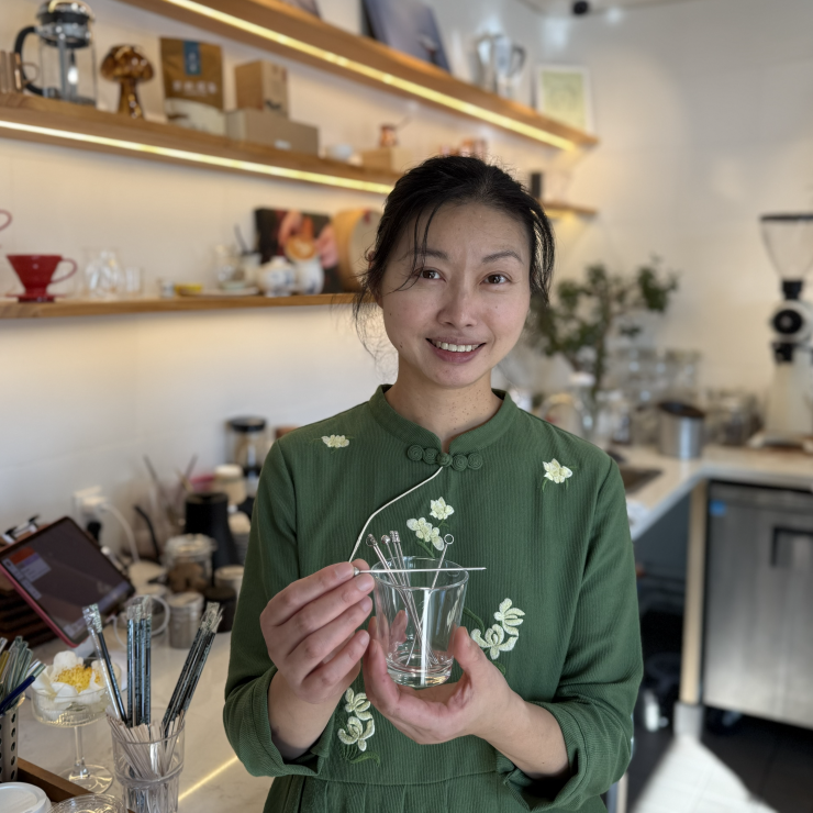 Cafe owner showing off reusable coffee cup and stirrer