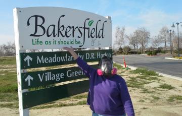 Person in filtering industrial face mask standing next to welcome sign for Bakersfield CA (Life as it should be)