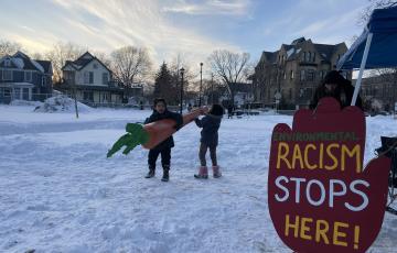 Two children carrying a large carrot to a demonstration next to a sign that says "racism stops here"
