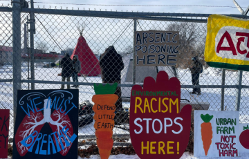 Environmental justice signs on fence: Racism Stops Here, Urban Farm not Toxic Harm