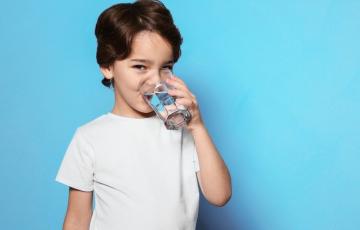Image of a boy in a white t-shirt drinking a glass of water. Source: canva