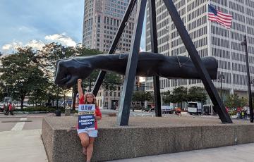 Joe Lewis fist statue in Detroit with UAW member holding her own fist up holding sign saying UAW Saving The American Dream