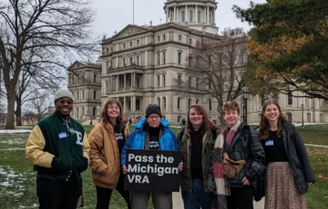 Group of people by Michigan Capitol holding sign "Pass the Michigan VRA"