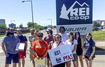 MN staff and members outside REI store sign with handmade "REI ban PFAS!" sign