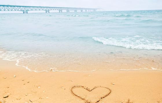 Heart in sand drawn in front of Straits with Mackinac Bridge in background. Credit Jennifer Schlicht