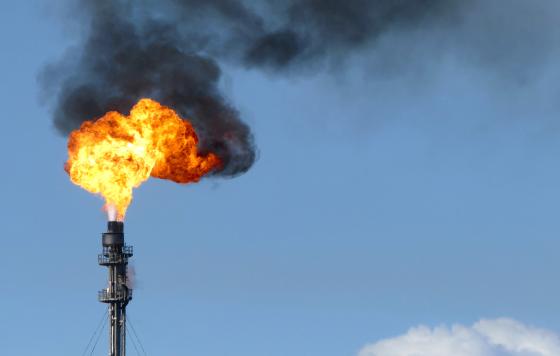 Gas flare fire and black smoke on blue sky day. 