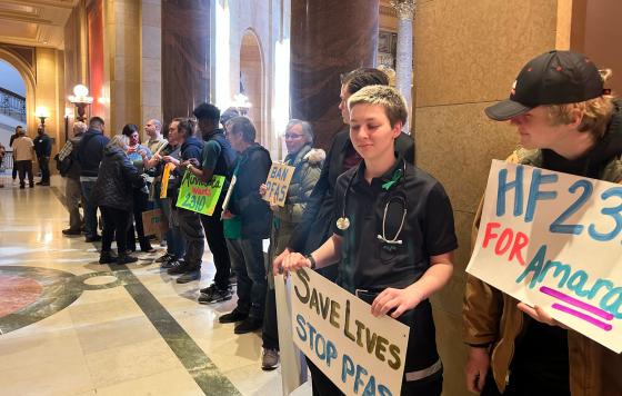 Line of people with signs outside Minnesota legislature: "Save Lives, Stop PFAS" "For Amara"