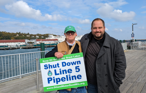 Sean McBrearty and Bill Latka holding a Shut Down Line 5 signs next to Mackinac Island