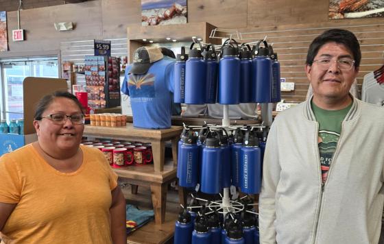 Two employees pose near a rack of reusable water bottles for sale in a gift shop