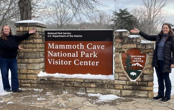 Two women next to the sign for the Mammoth Cave National Park Visitor Center