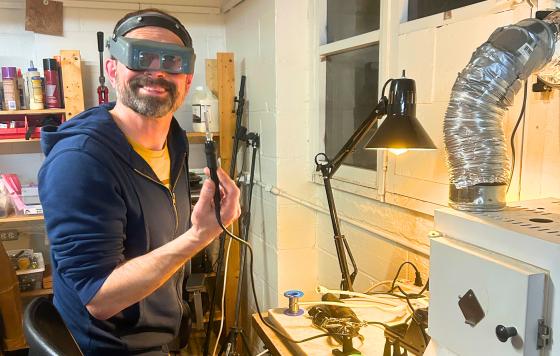 A volunteer wearing safety glasses posing in front of a electronics repair project