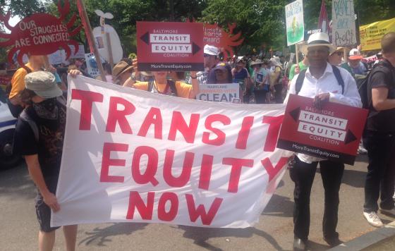 Supporters of the Baltimore Transit Equity Coalition hold a sign that reads "Transit Equity Now"