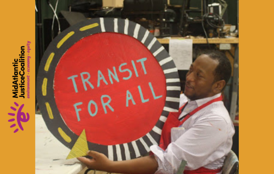 A picture of someone having just finished painting a round sign that says "Transit for All"
